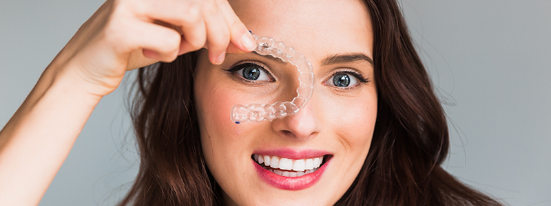 A woman showcasing clear aligners, also known as Invisalign aligners, in her hand.