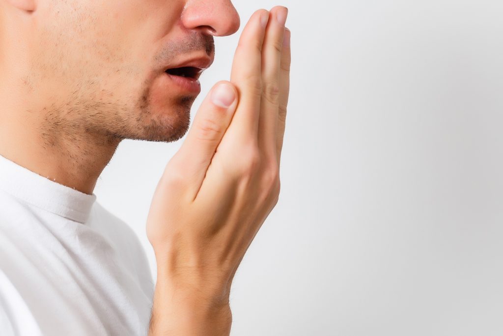 Photo of a man holding up his palm, grimacing in discomfort, experiencing halitosis.