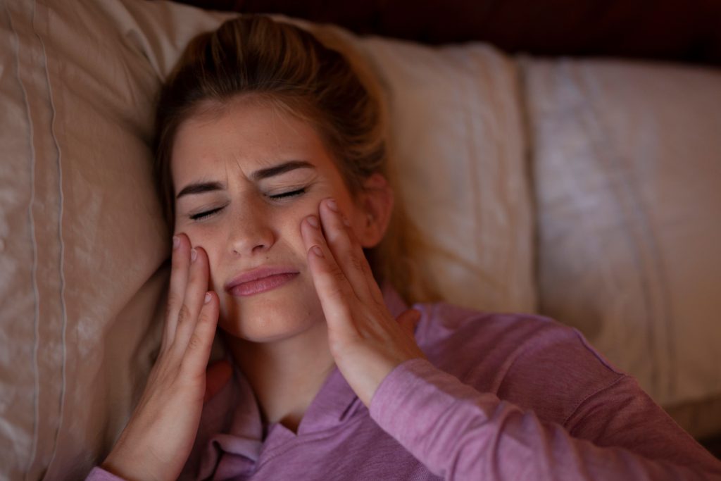 Image shows a woman with hands on her face, sleeping with teeth grinding.