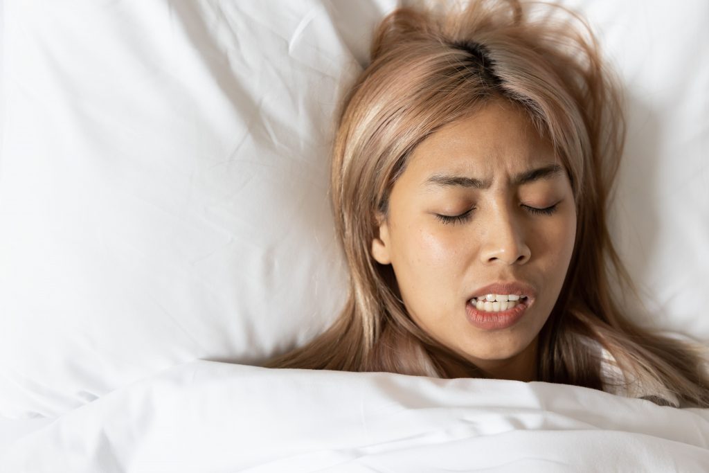 A woman sleeping peacefully in bed, mouth open, with teeth grinding.