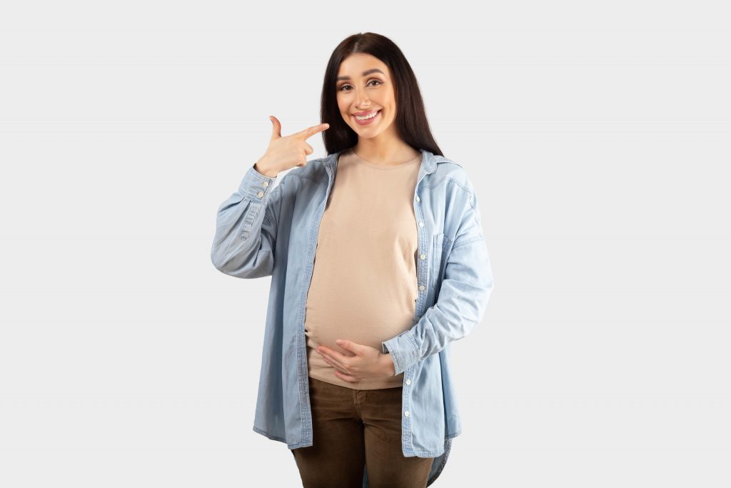 A pregnant woman smiling and pointing her teeth with her hand