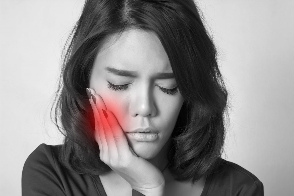 A close-up image of a person holding their cheek in pain, indicating a toothache.