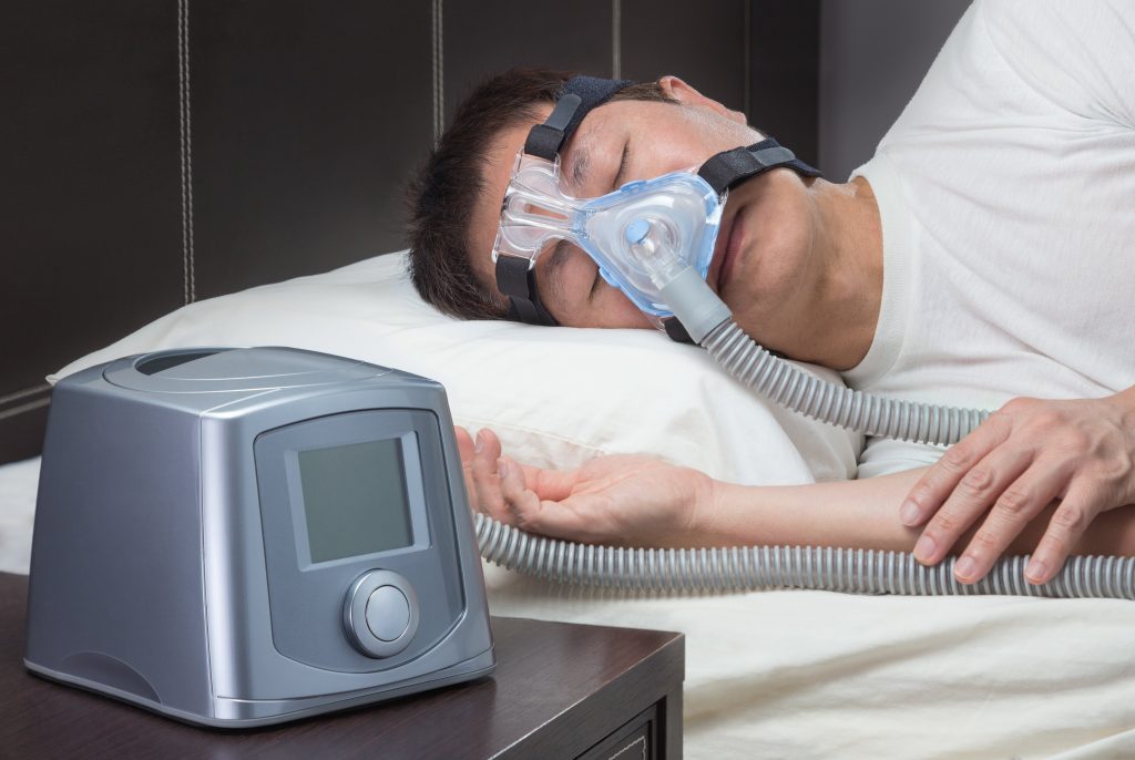 Image of a man experiencing sleep apnea, using an oxygen mask while sleeping.