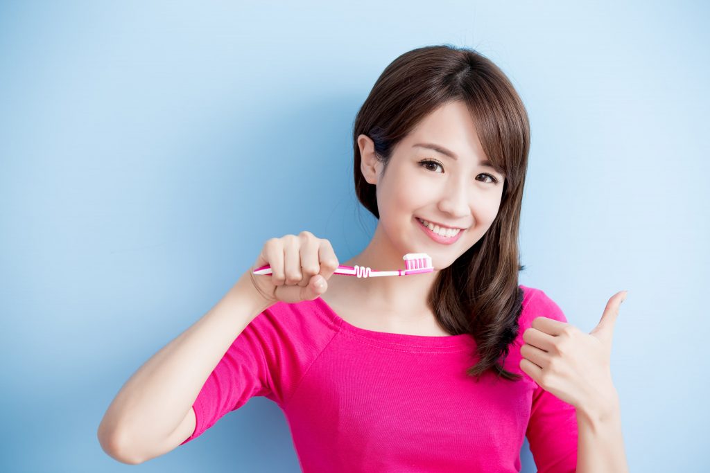 A woman holding a toothbrush and showing approval with a thumbs up gesture.