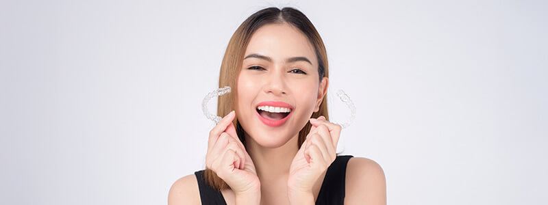 Smiling woman holding Invisalign clear aligners in both hands